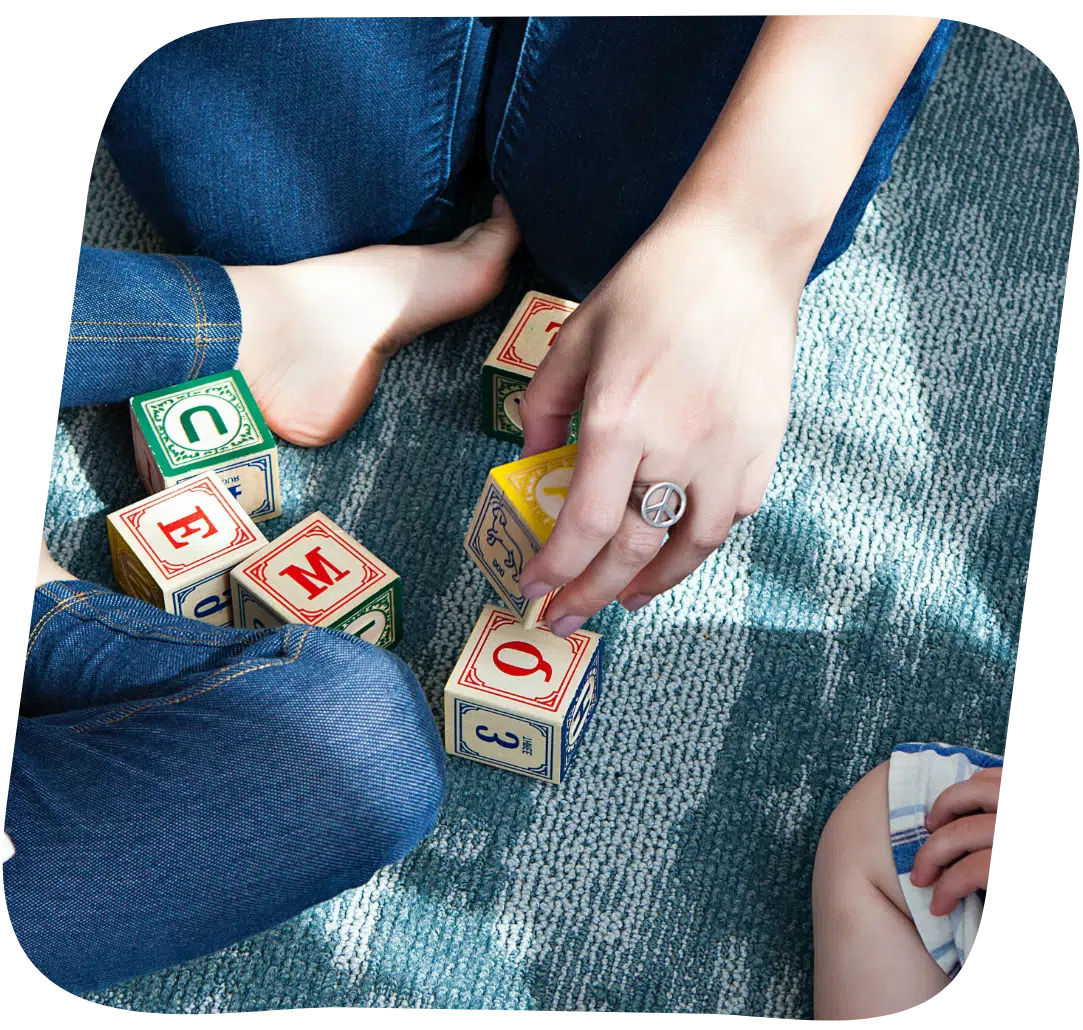 A woman engaging a child with toy blocks and wearing a peace symbol ring