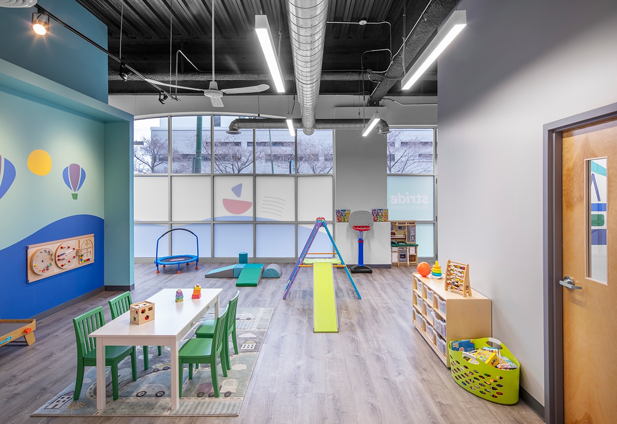 View of interior open space with toys, seating area, windows and a door at the Stride Autism Center near Belmont Heights in Chicago, Illinois.