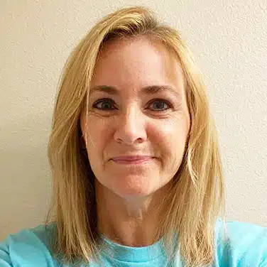Photo of a woman with straight hair and curtain bangs who is looking straight at the camera and is flashing a closed-lipped smile.
