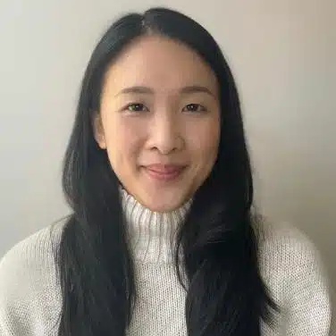Headshot of a woman wearing a turtleneck top, flashing a close-lipped smile at the camera.