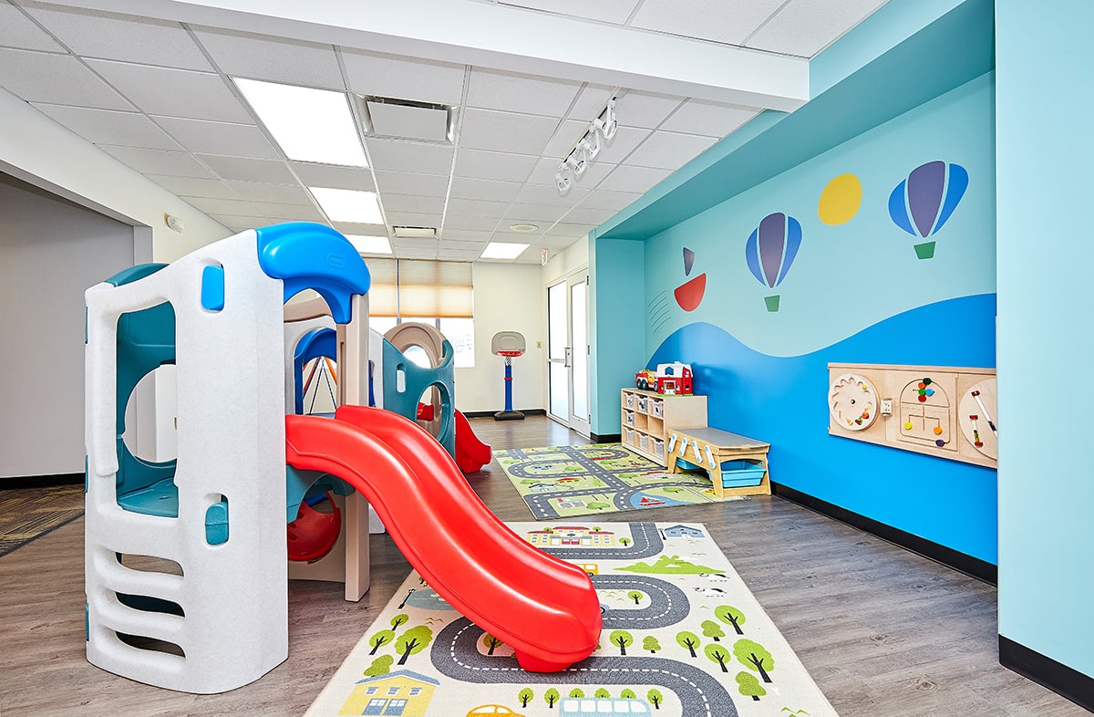 View of interior open space with toys, slide, windows and a door at the Stride Autism Center in Lincoln, Nebraska.