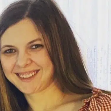 Headshot of a woman with straight hair, flashing a smile while looking straight at the camera. Shot is tilted to the left.