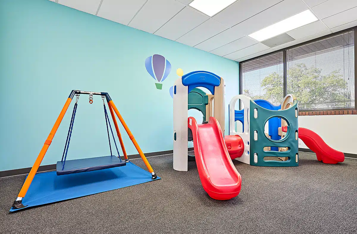 View of interior open space with toys, a table, and windows at the Stride Autism Center near Fort Calhoun, Nebraska.