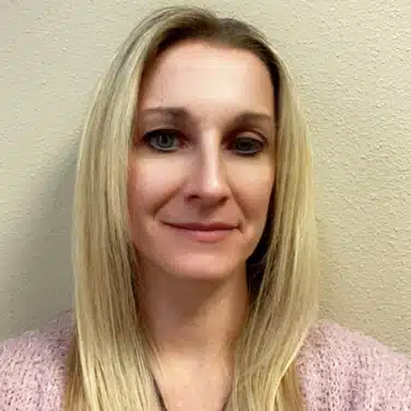 Headshot of a woman with straight hair, flashing a small close-lipped smile while looking straight at the camera.