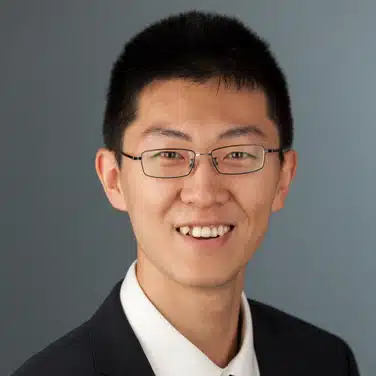 Headshot of a man with square-rimmed eyeglasses, flashing a smile while looking straight at the camera.