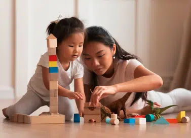 Photo of a toddlers and a woman playing wooden blocks.