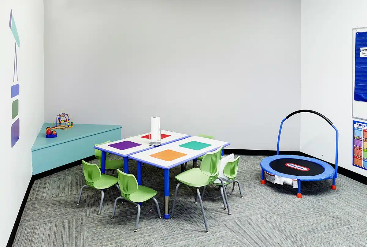 Photo of a play area with a trampoline, table, chairs, toys, and a roll of paper towel on the table.