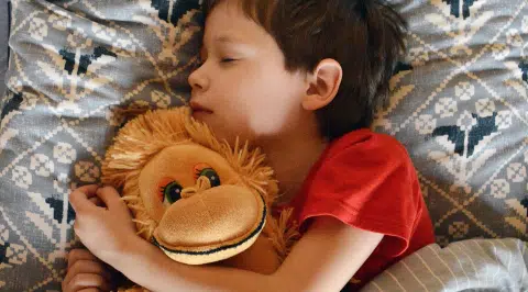 Un niño durmiendo con un peluche de mono.