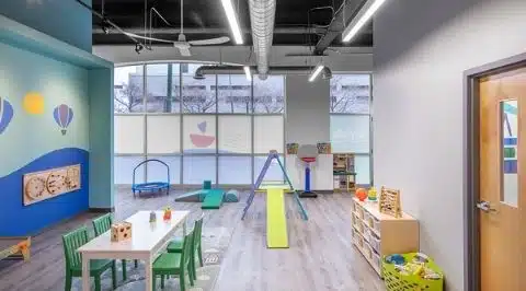 Un miembro del personal profesional del Stride Autism Center sonríe cálidamente en el ambiente luminoso y acogedor de la clínica de terapia.